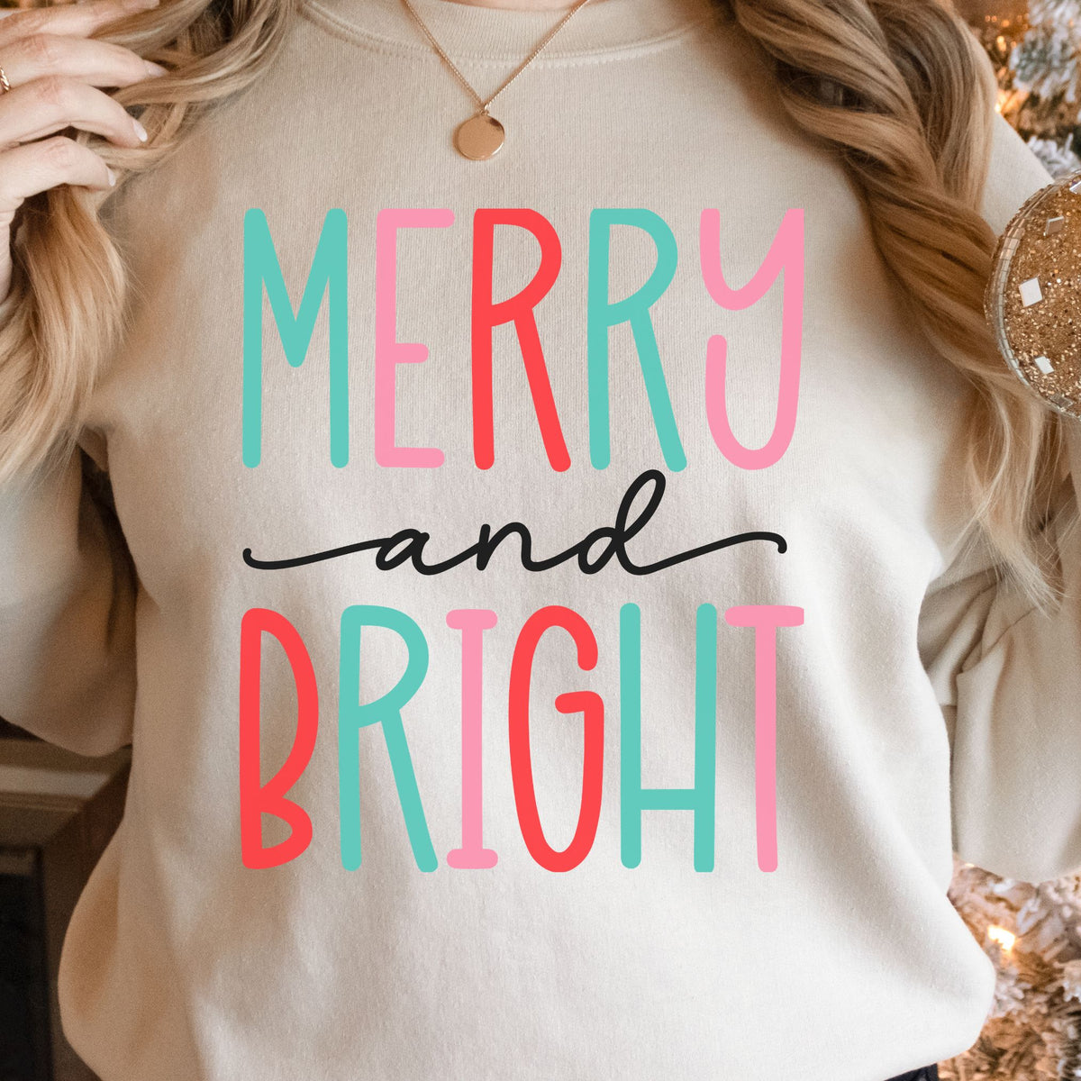 Woman wearing a sand sweatshirt with a colorful Merry and Bright design.