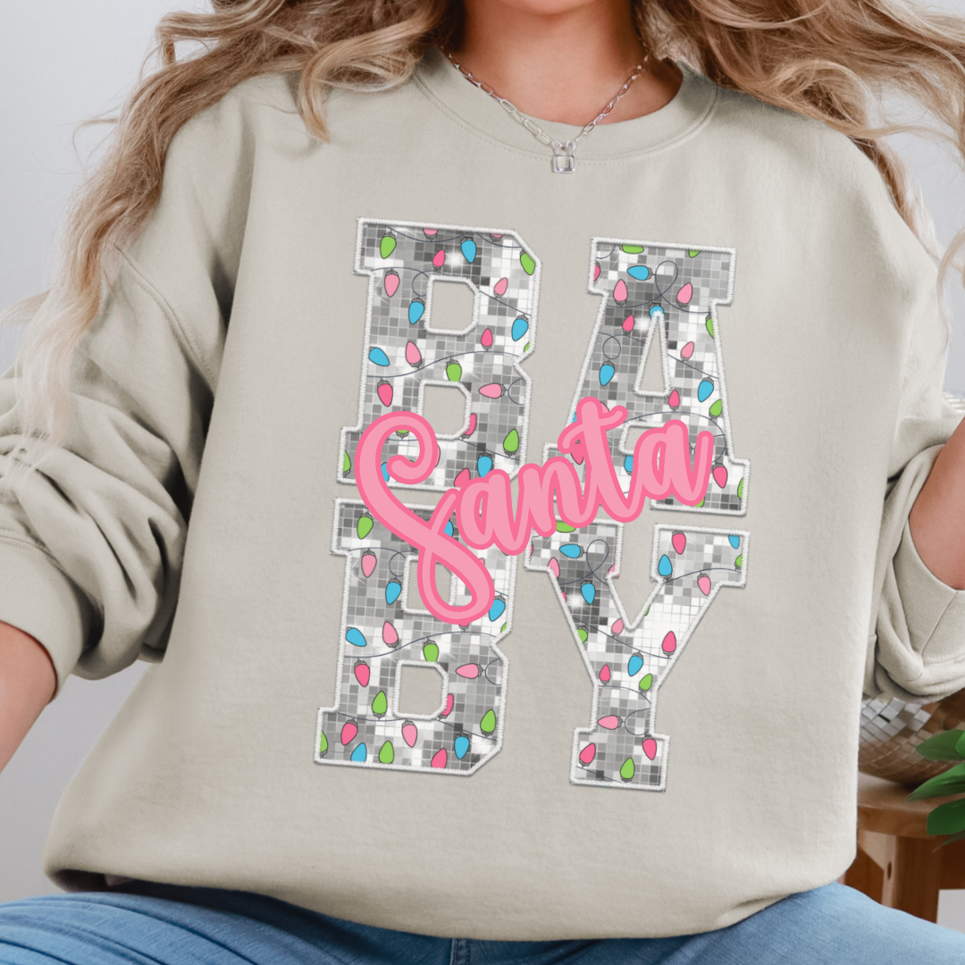 Woman wearing a sand sweatshirt with a Santa Baby Christmas lights design.