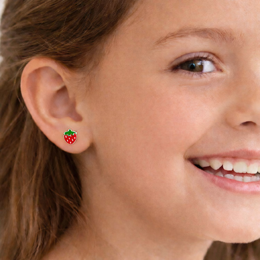 A young girl with a bright smile is wearing a pair of red strawberry earrings.