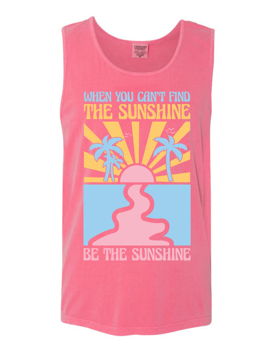A pink tank top with a graphic design featuring a sun, palm trees, and a message encouraging the wearer to "Be the sunshine".