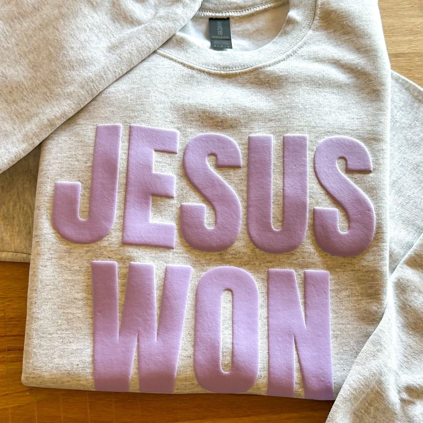 A grey sweatshirt with the text "JESUS WON" printed in large purple letters.
