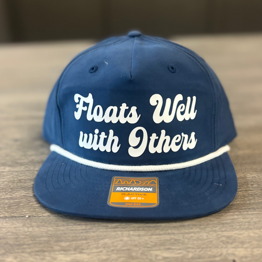 A navy blue baseball cap with white text that says "Floats Well with Others" on it.