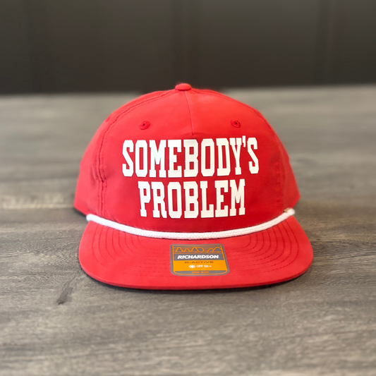 A red baseball cap with the text "SOMEBODY'S PROBLEM" printed on it.