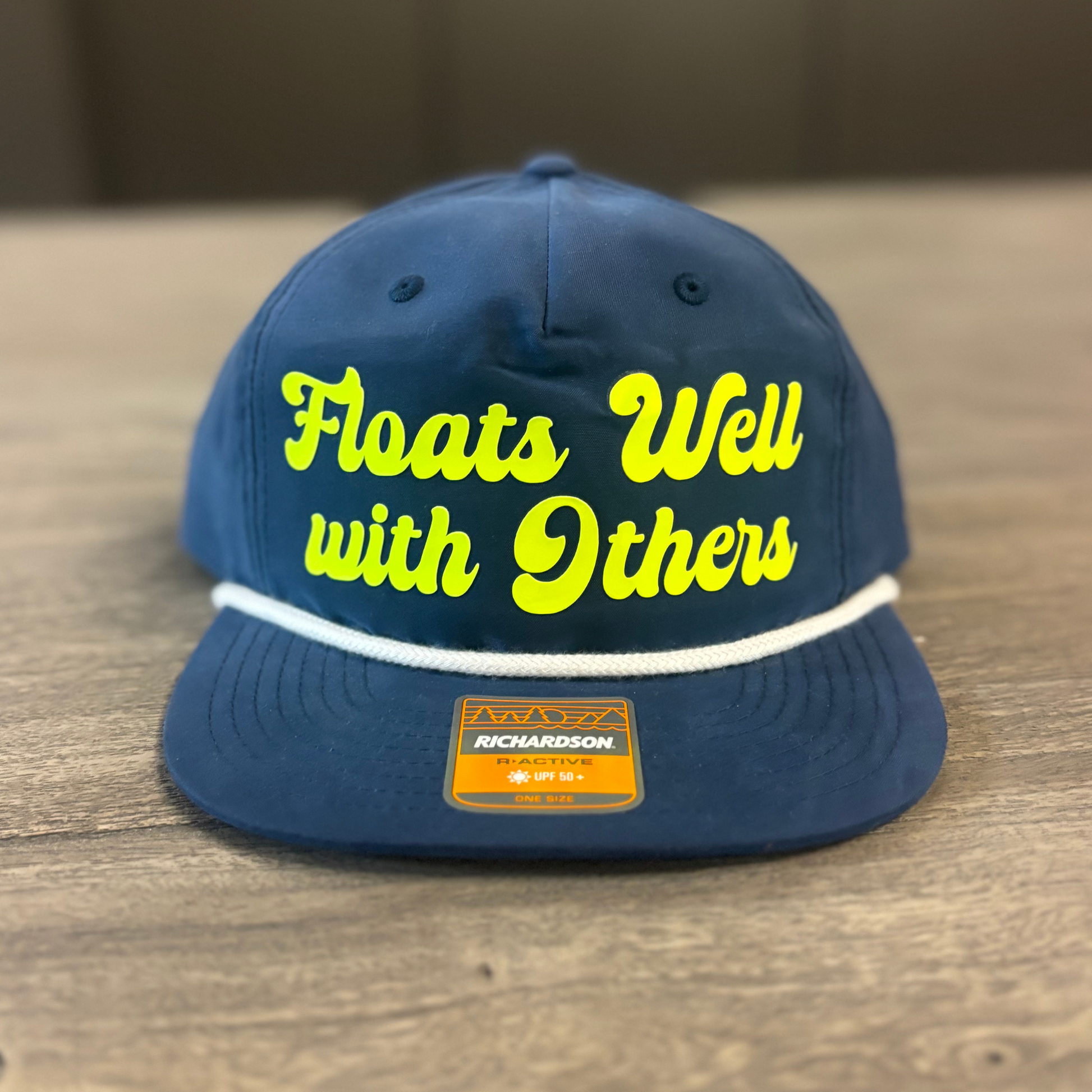 A navy blue baseball cap with yellow text that says "Floats Well with Others" on it.