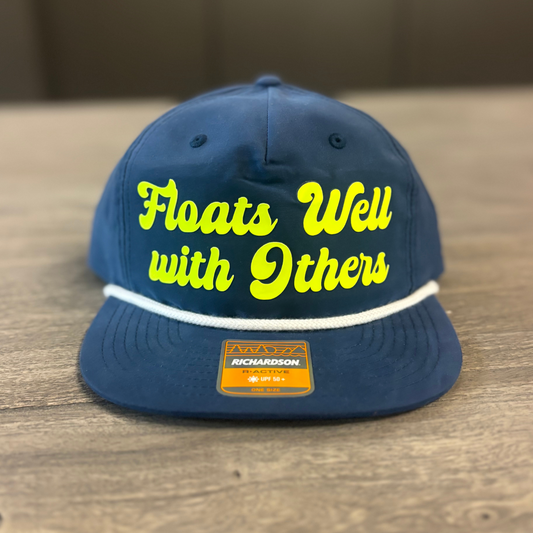 A navy blue baseball cap with yellow text that says "Floats Well with Others" on it.