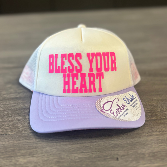 A white baseball cap with pink text that says "Bless Your Heart" on it.