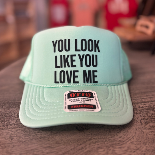 A light green baseball cap with the text "YOU LOOK LIKE YOU LOVE ME" printed on it.