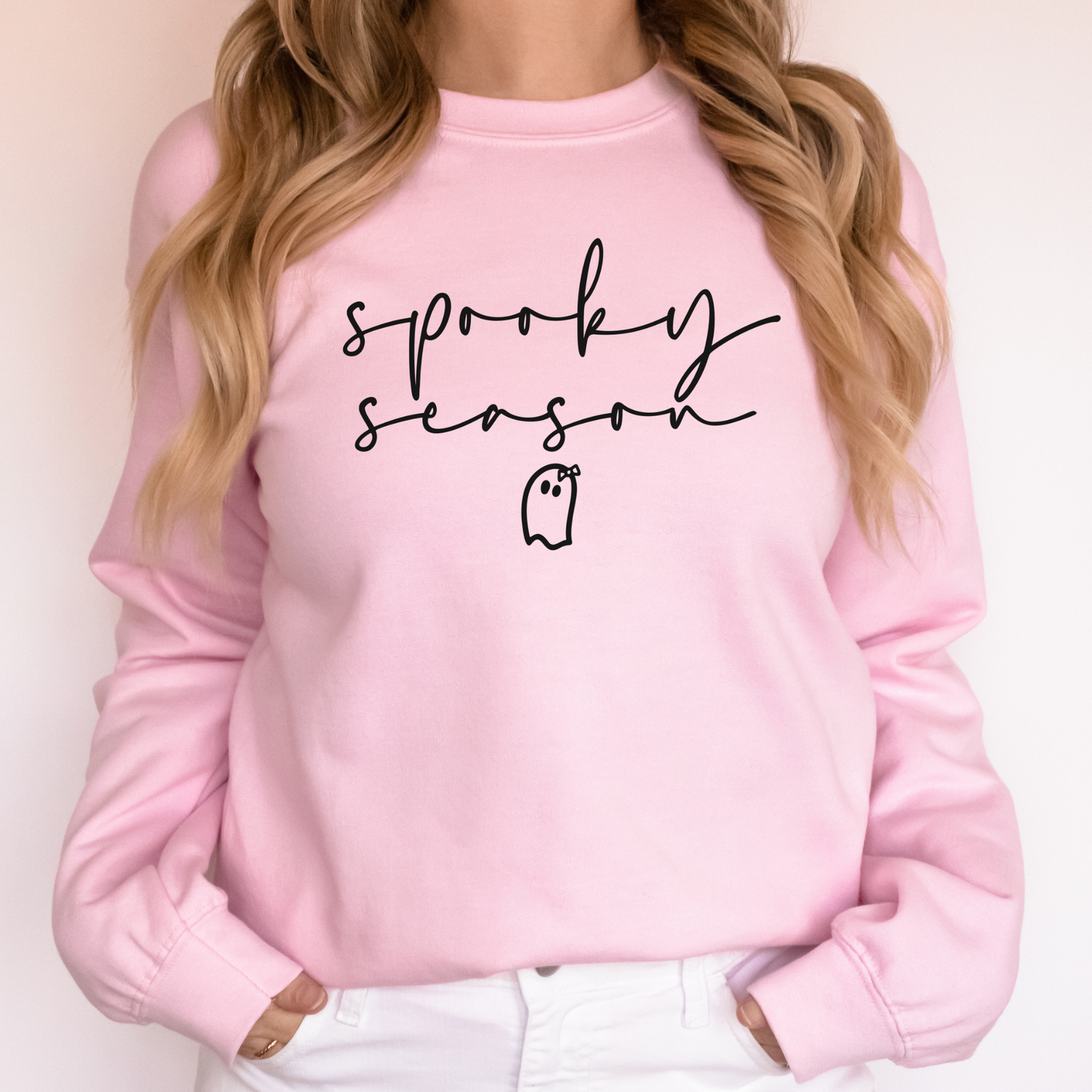 a woman wearing a pink sweatshirt with the words spooky season written on it