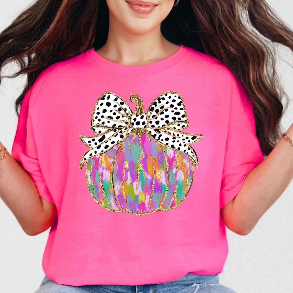 Colorful painted pumpkin with spotted bow on a Neon Pink Comfort Colors 1717 T-shirt
