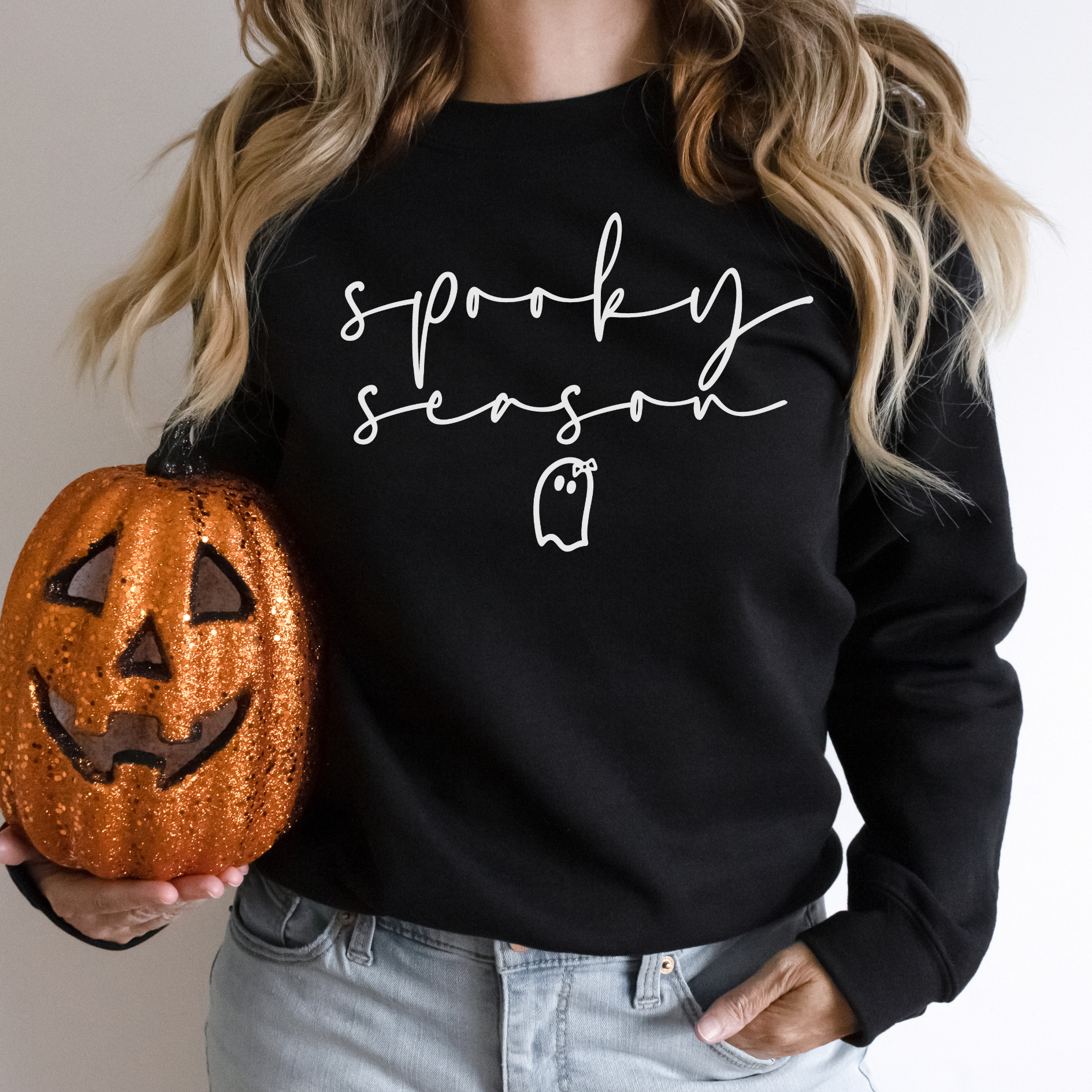 a woman in a black sweatshirt holding a pumpkin