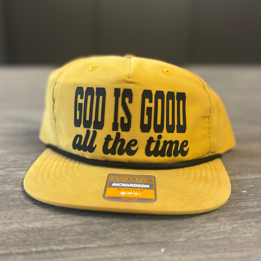 A yellow baseball cap with the text "GOD IS GOOD all the time" printed on it.