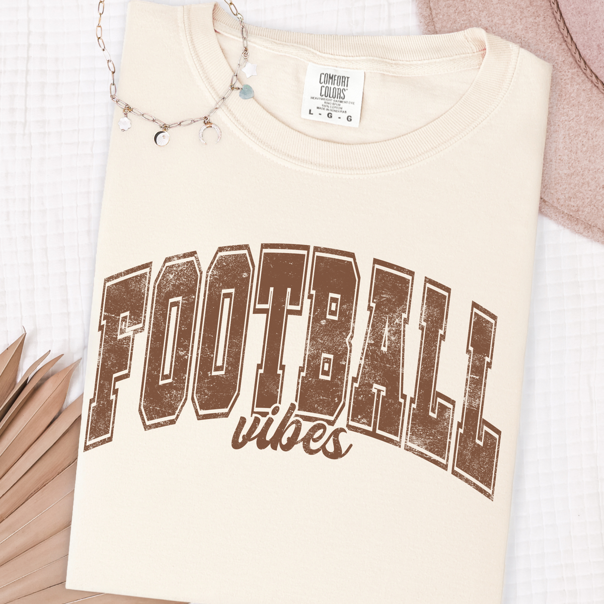 Folded ivory Comfort Colors 1717 T-shirt with distressed brown Football Vibes design