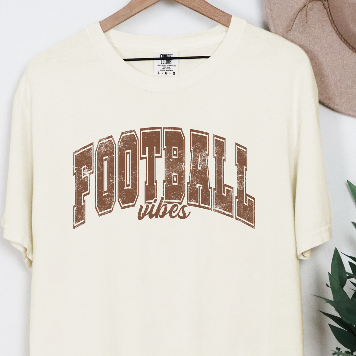 Ivory Comfort Colors 1717 Football Vibes graphic T-shirt hanging on a wooden hanger