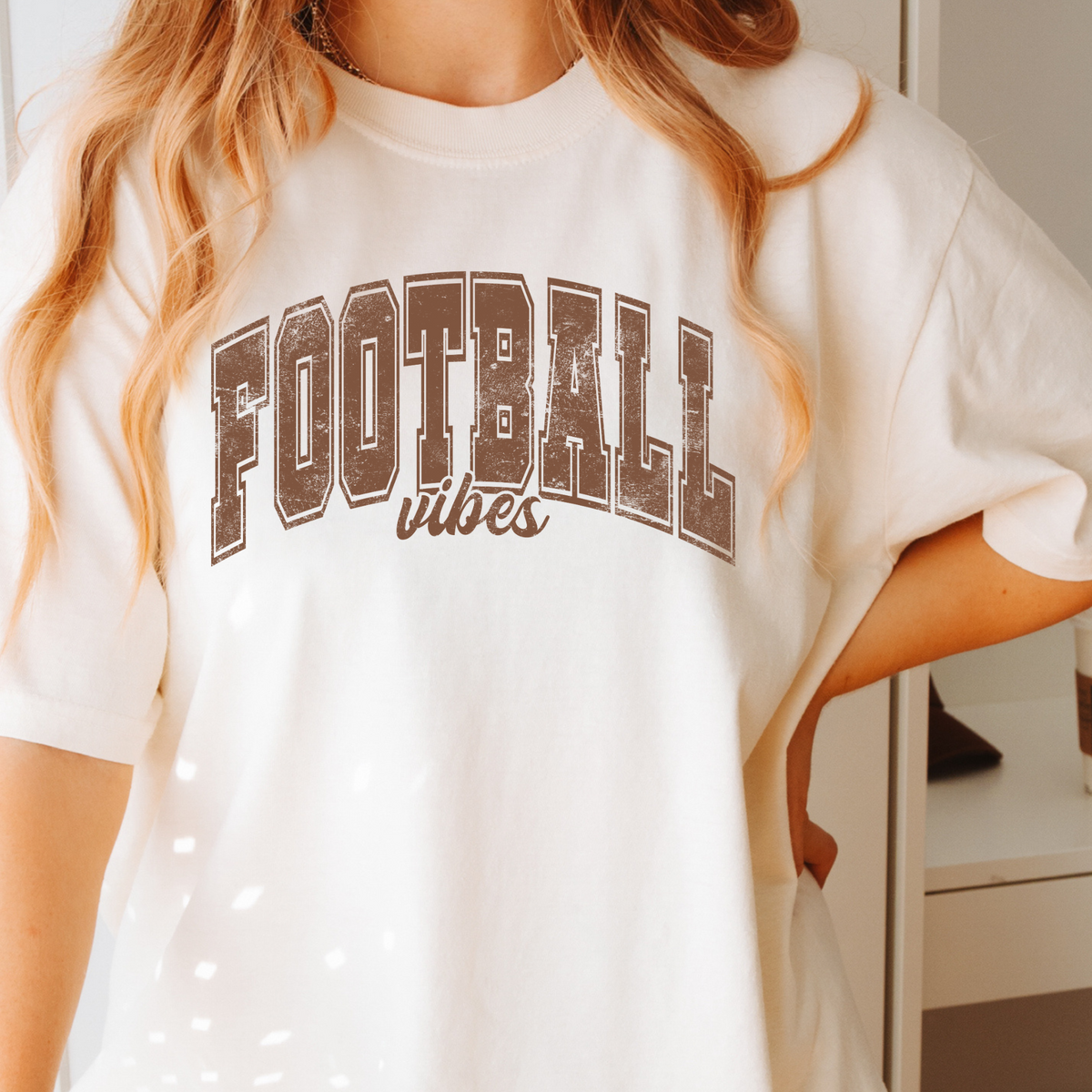 Woman wearing an ivory Comfort Colors 1717 T-shirt with brown Football Vibes design