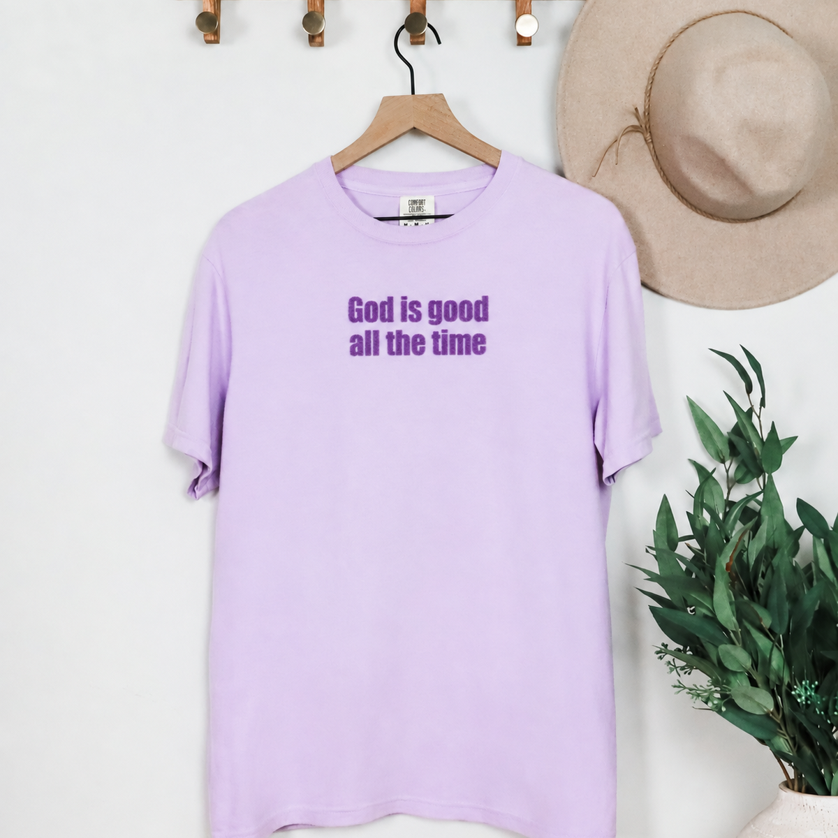 Orchid God Is Good All the Time Christian T-shirt hanging on a wooden hanger