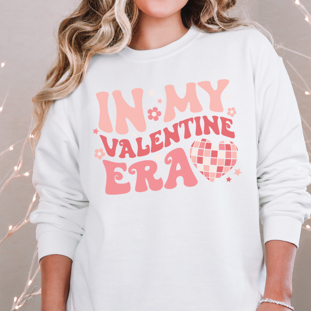Woman wearing a white In My Valentine Era graphic sweatshirt.