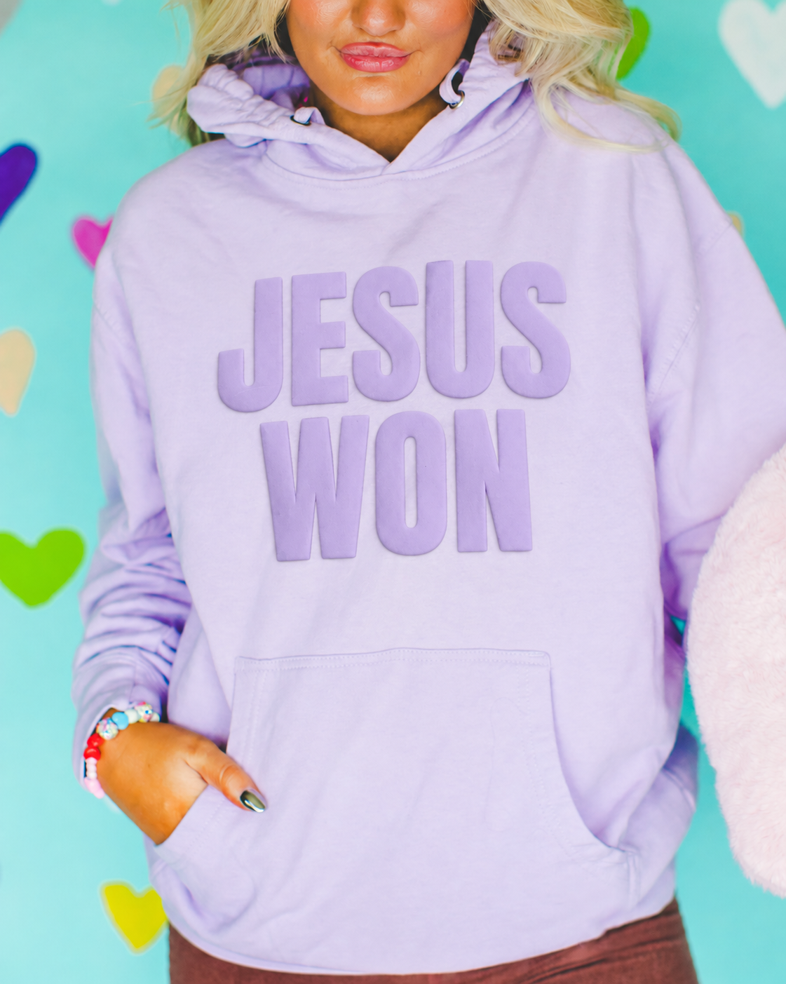 Woman wearing a lavender hoodie with raised lavender "Jesus Won" lettering.