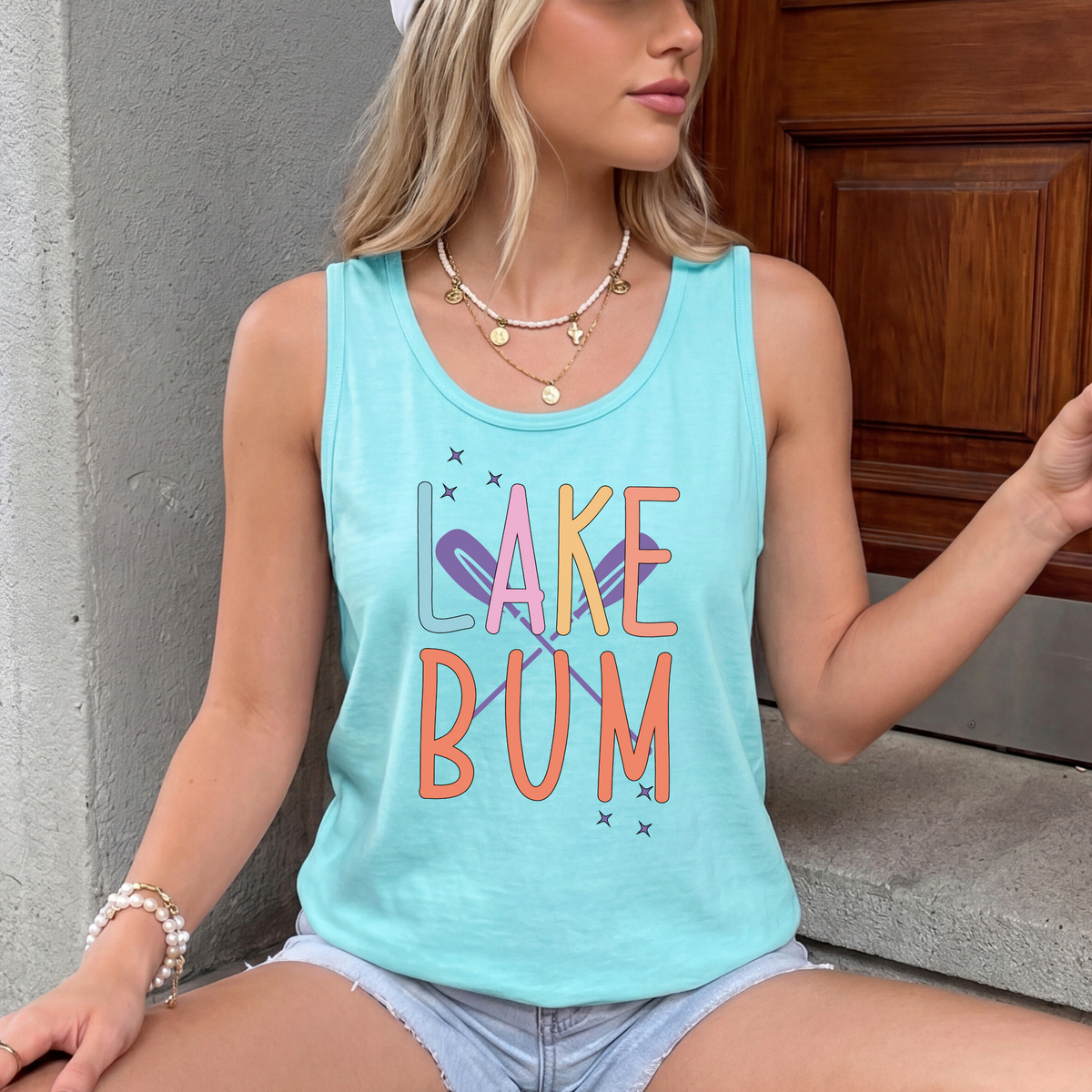 Pastel LAKE BUM lettering with crossed purple oars and stars on a Chalky Mint tank top.