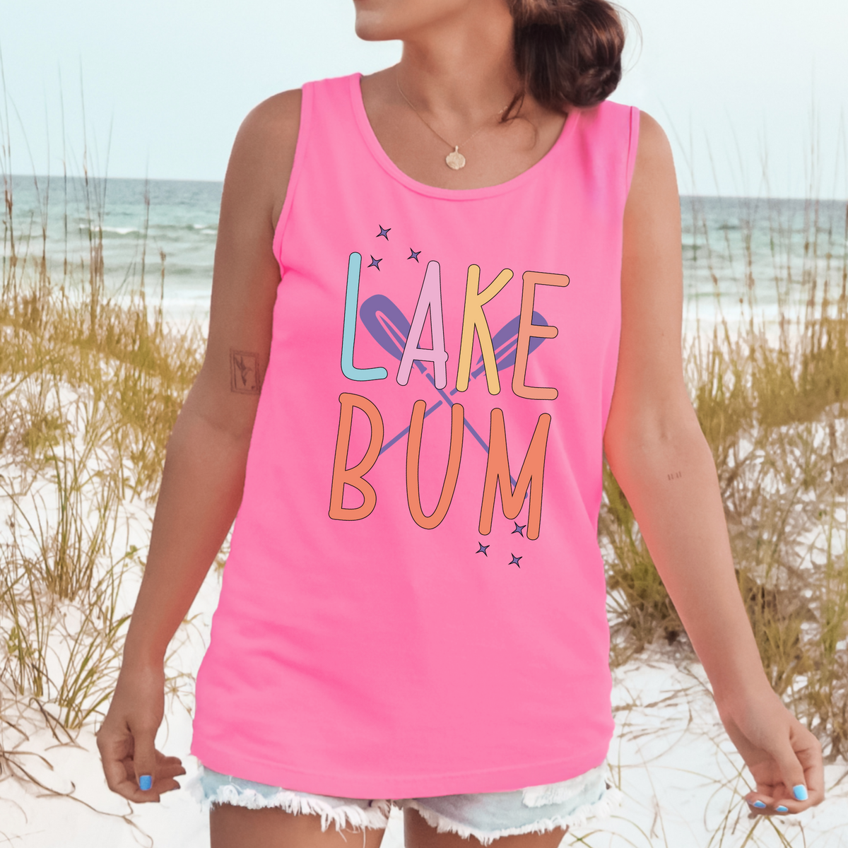 Pastel LAKE BUM lettering with crossed purple oars and stars on a Neon Pink tank top.