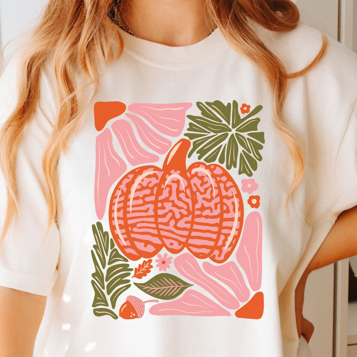 Light pink and orange patterned pumpkin with olive green autumn leaves on a Ivory T-shirt