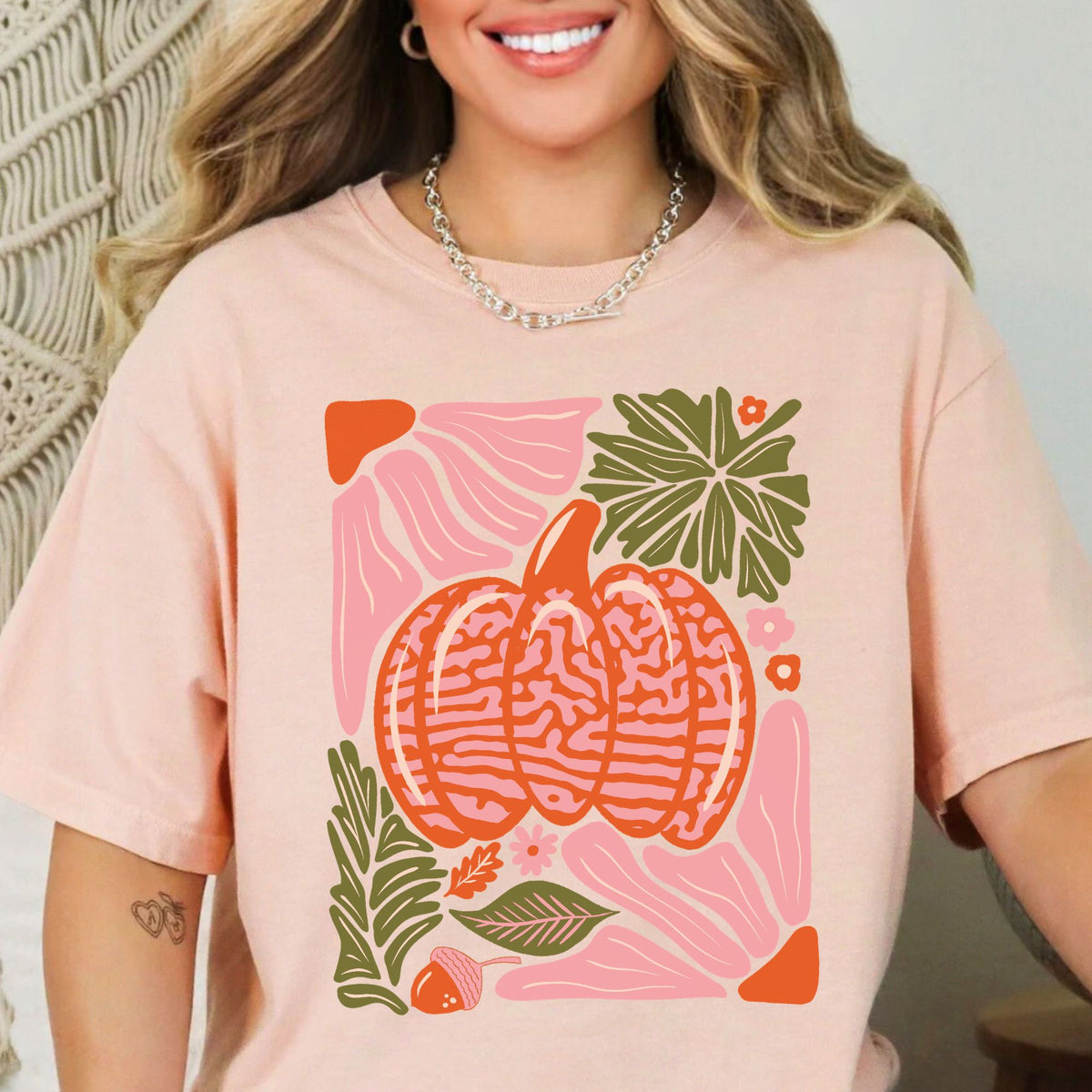 Light pink and orange patterned pumpkin with olive green autumn leaves on a Peachy T-shirt
