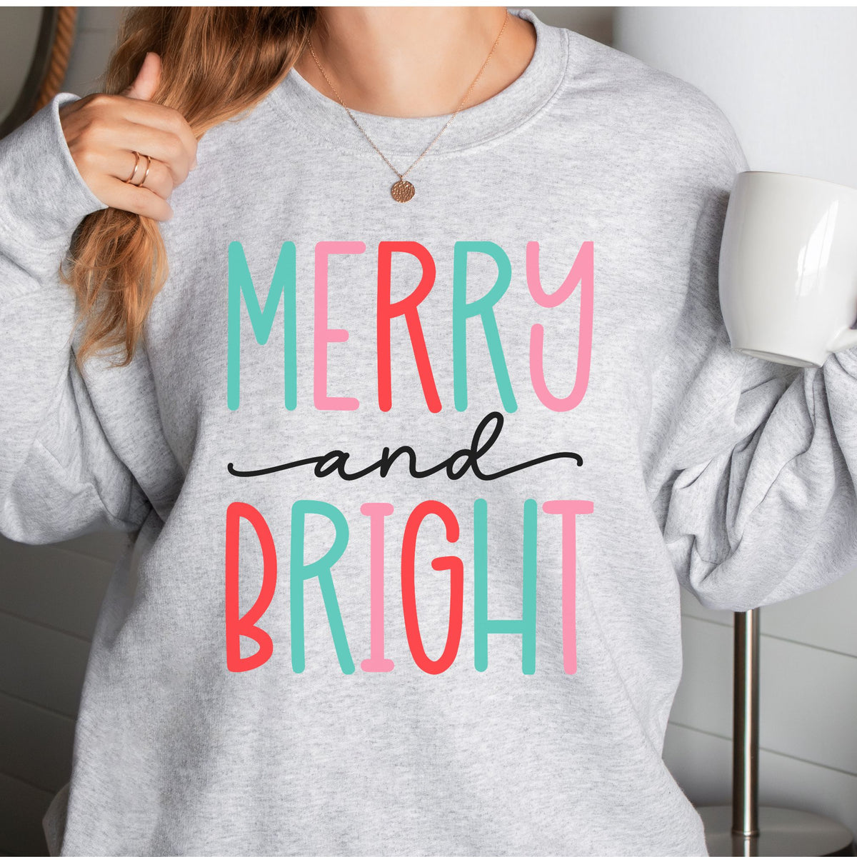 Woman wearing an ash sweatshirt with a colorful Merry and Bright design.