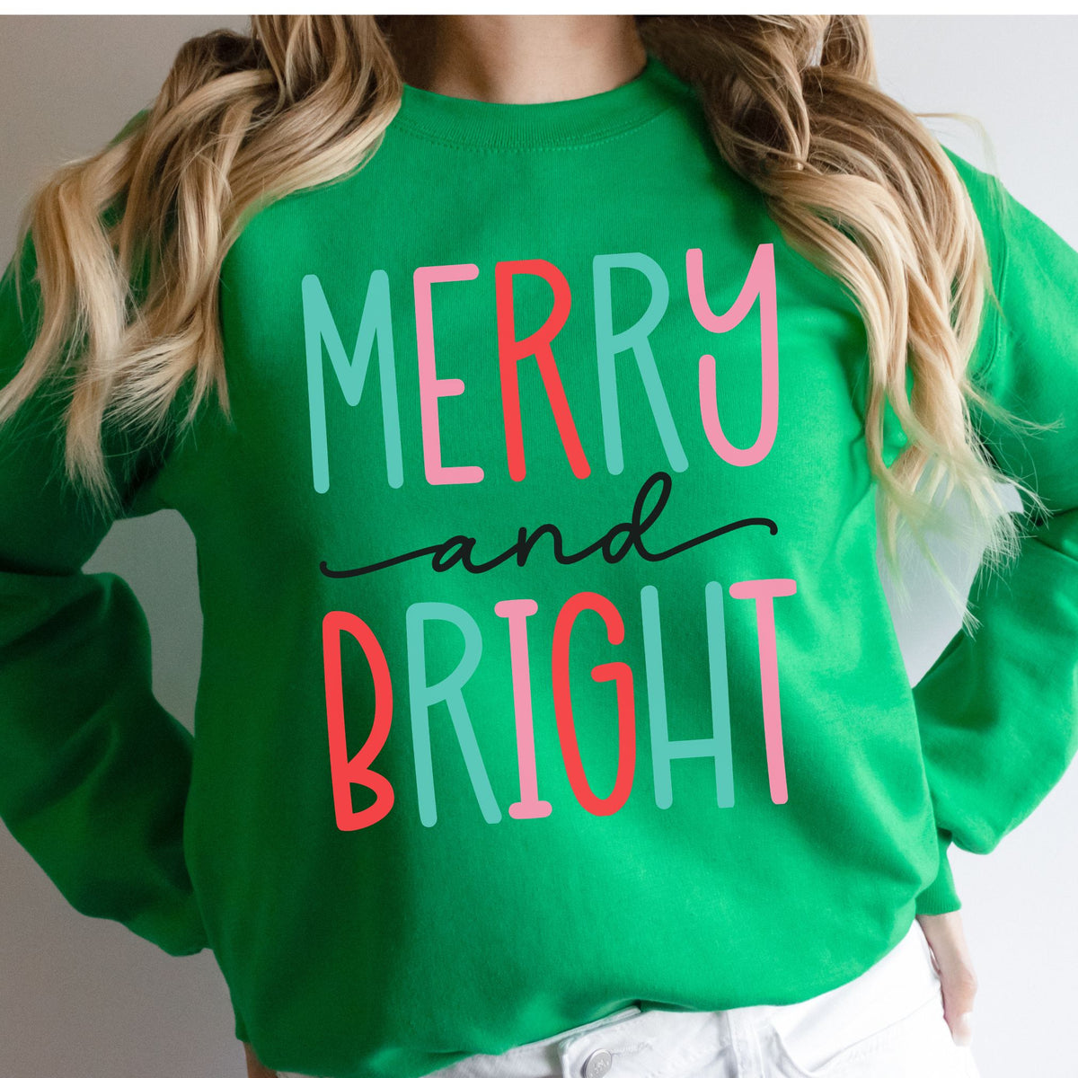 Woman wearing a green sweatshirt with a colorful Merry and Bright design.