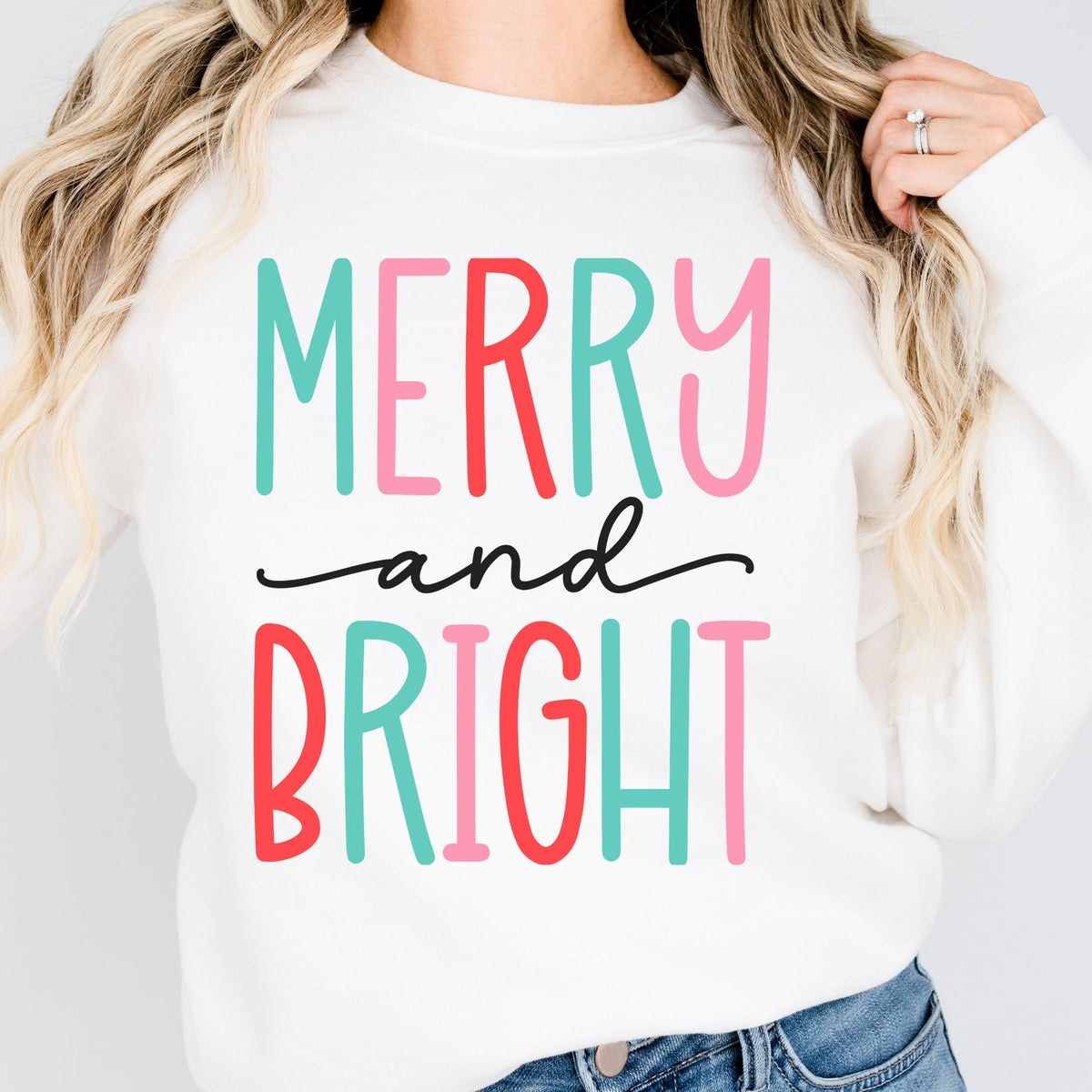 Woman wearing a white sweatshirt with a colorful Merry and Bright design.