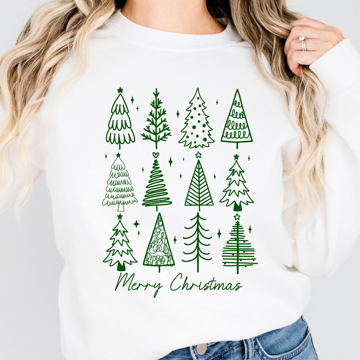 Woman wearing a white sweatshirt with green doodle Christmas trees and Merry Christmas text.