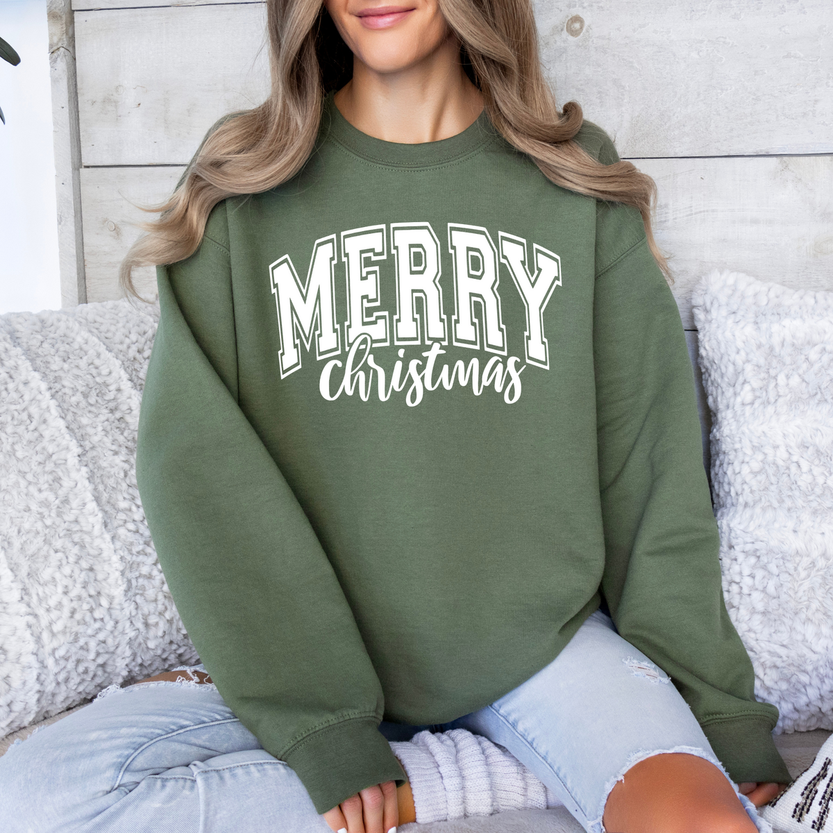 Woman wearing a heather dark green sweatshirt with a white Merry Christmas collegiate design.