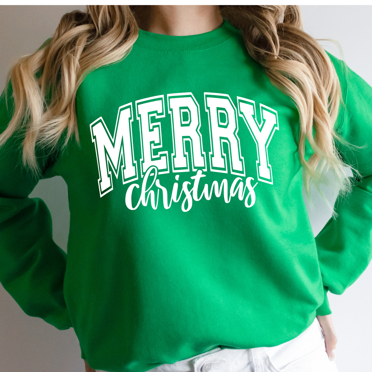 Woman wearing an Irish green sweatshirt with a white Merry Christmas collegiate design.
