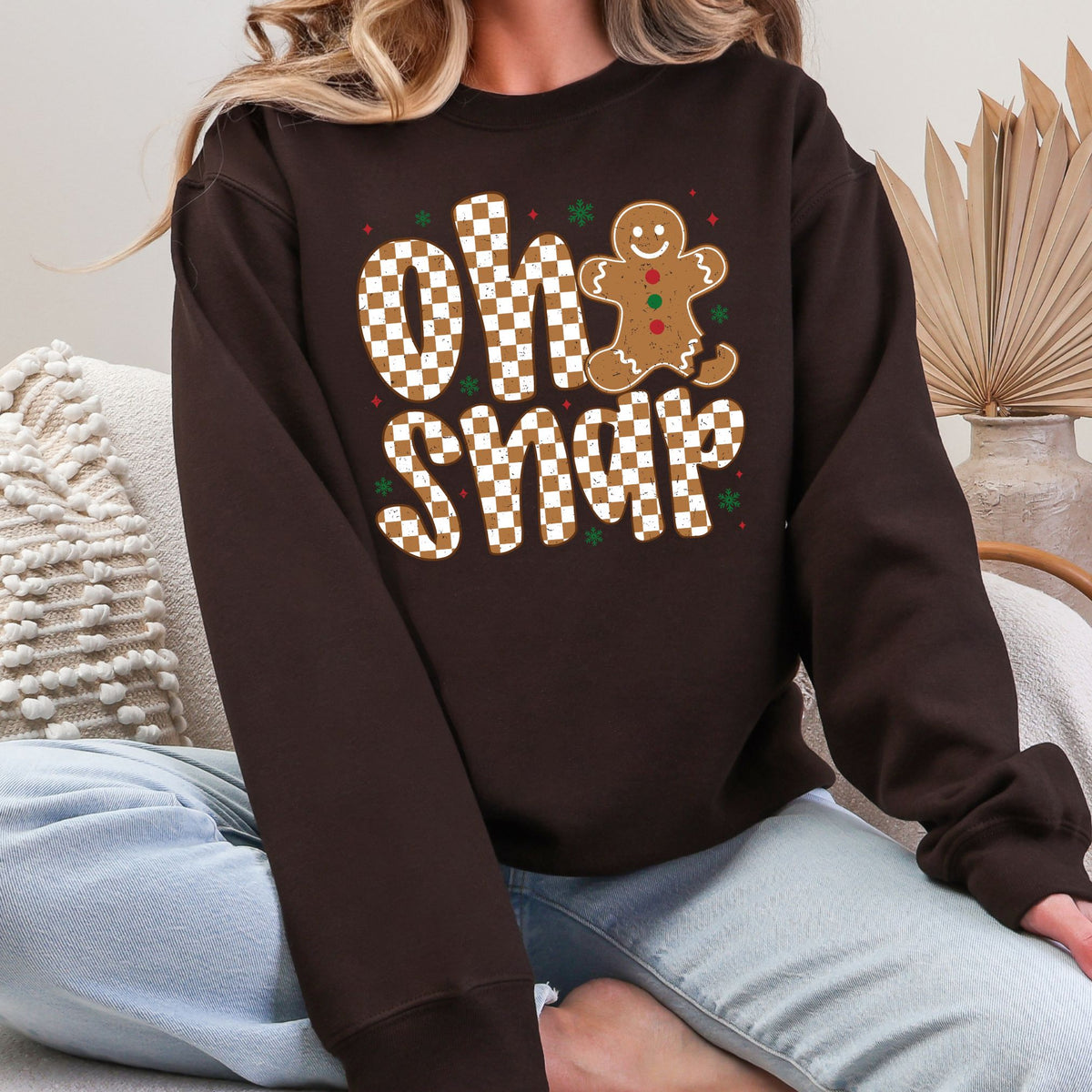 Woman wearing a dark chocolate sweatshirt with a checkered Oh Snap gingerbread design.