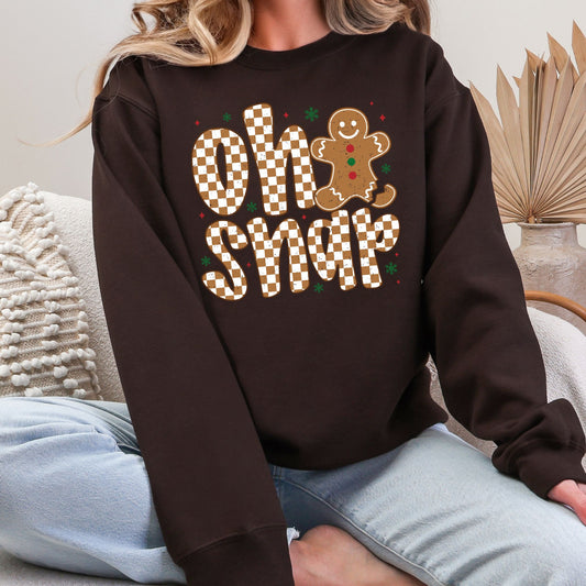 Woman wearing a dark chocolate sweatshirt with a checkered Oh Snap gingerbread design.