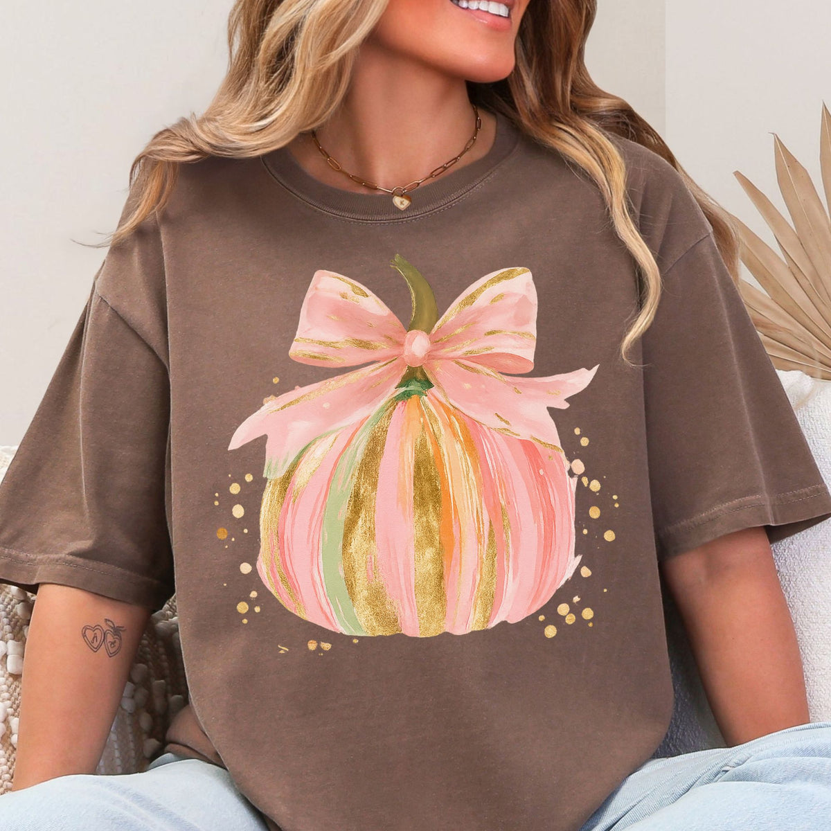 Pastel pink, orange, and green pumpkin with gold-look accents and a pink bow on a Espresso T-shirt