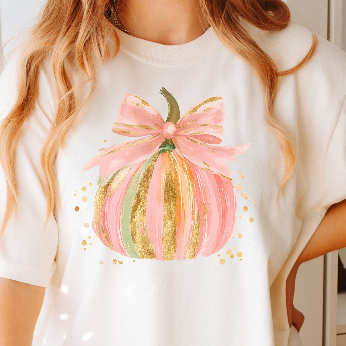 Pastel pink, orange, and green pumpkin with gold-look accents and a pink bow on a Ivory T-shirt