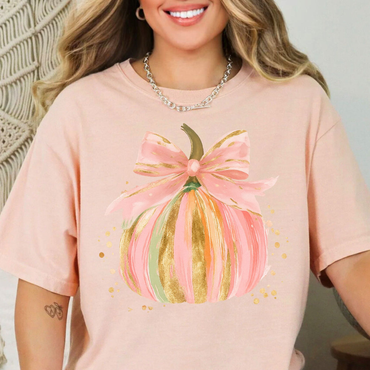 Pastel pink, orange, and green pumpkin with gold-look accents and a pink bow on a Peachy T-shirt