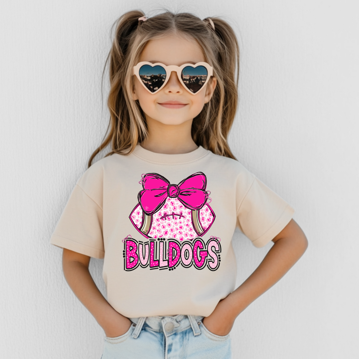 Girl wearing a Natural Bella Canvas 3001Y pink leopard football bow Bulldogs youth T-shirt