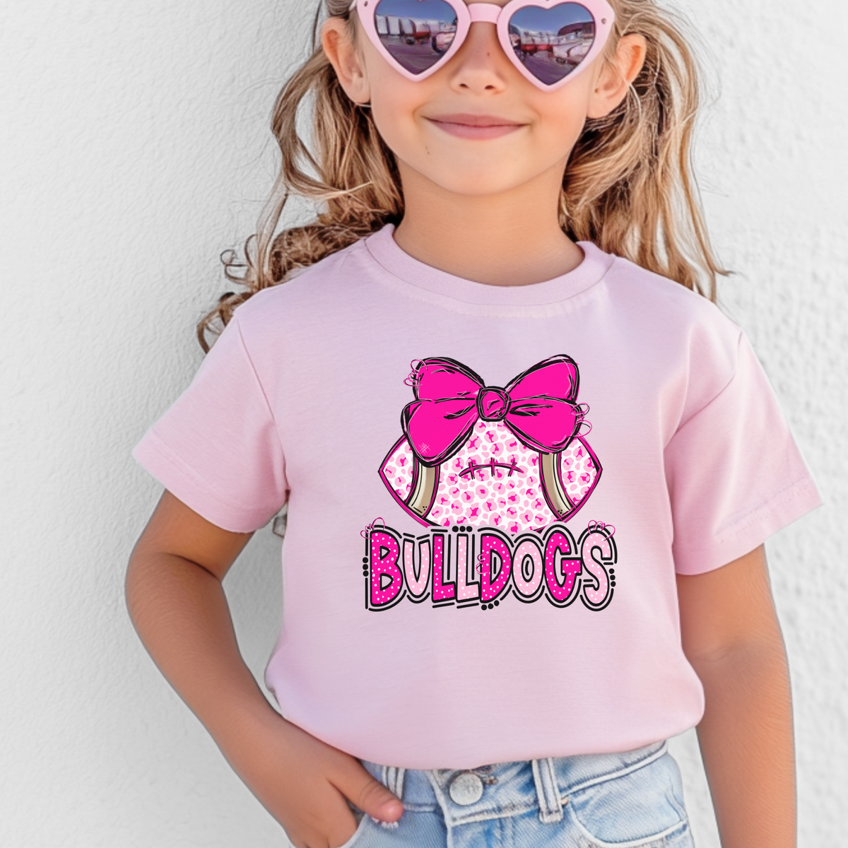 Girl wearing a Pink Bella Canvas 3001Y pink leopard football bow Bulldogs youth T-shirt