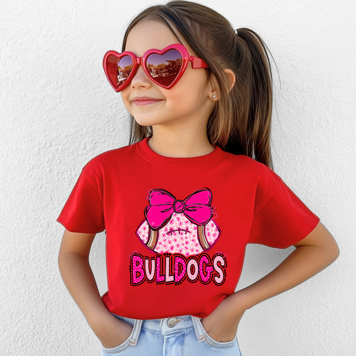 Girl wearing a Red Bella Canvas 3001Y pink leopard football bow Bulldogs youth T-shirt