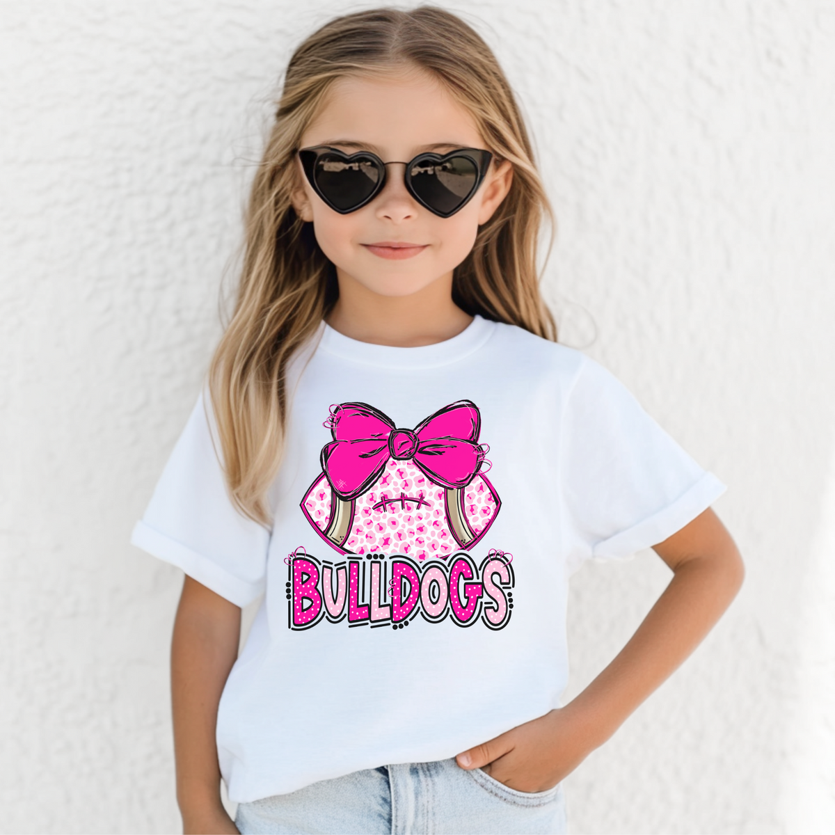 Girl wearing a White Bella Canvas 3001Y pink leopard football bow Bulldogs youth T-shirt