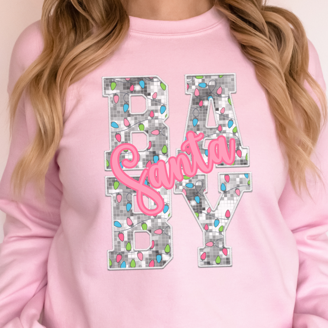Woman wearing a light pink sweatshirt with a Santa Baby Christmas lights design.