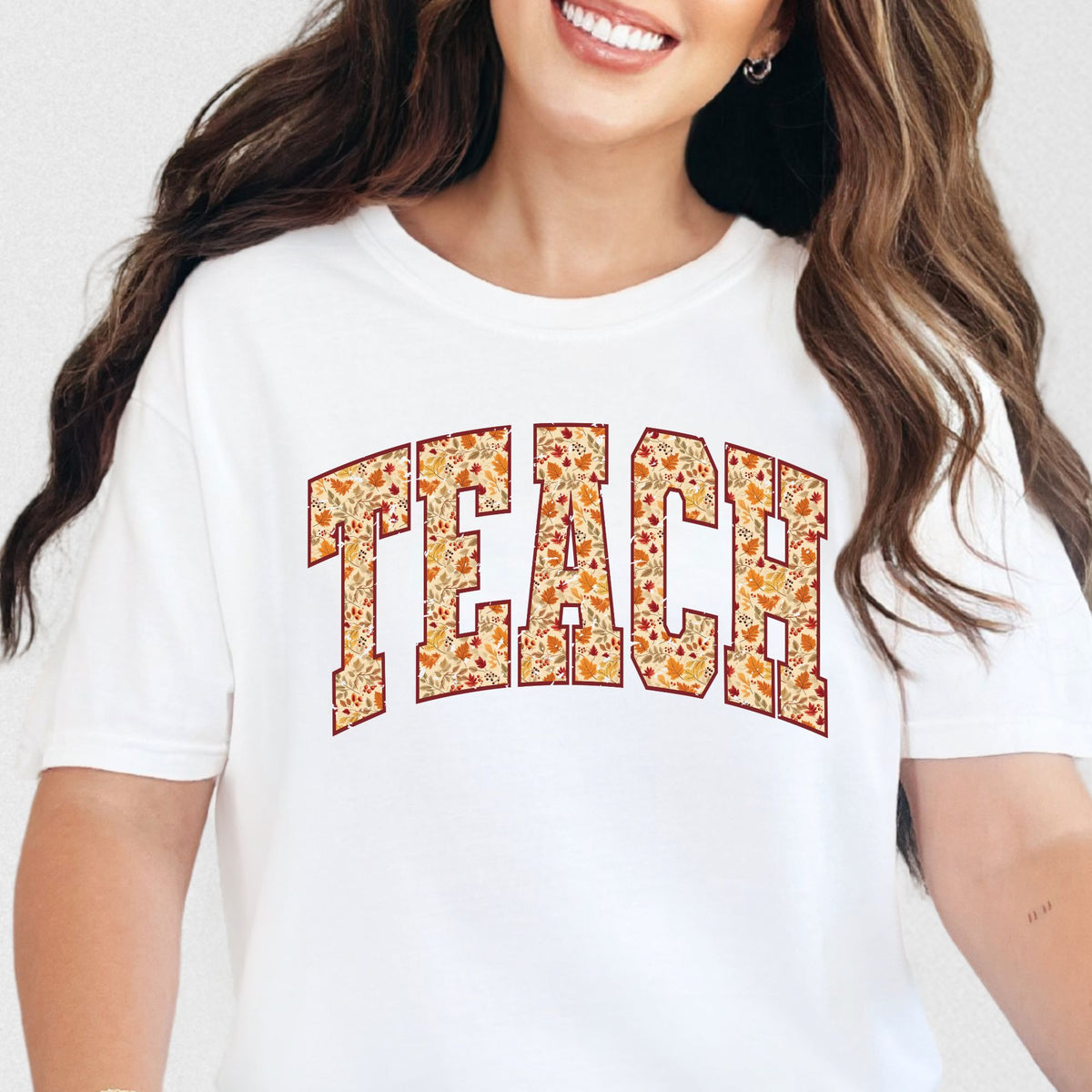 Woman wearing a White TEACH fall leaves graphic T-shirt