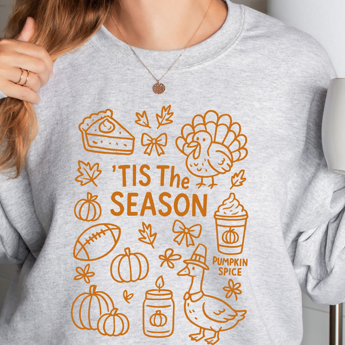 Woman wearing an Ash ’Tis the Season Thanksgiving sweatshirt with orange doodle artwork