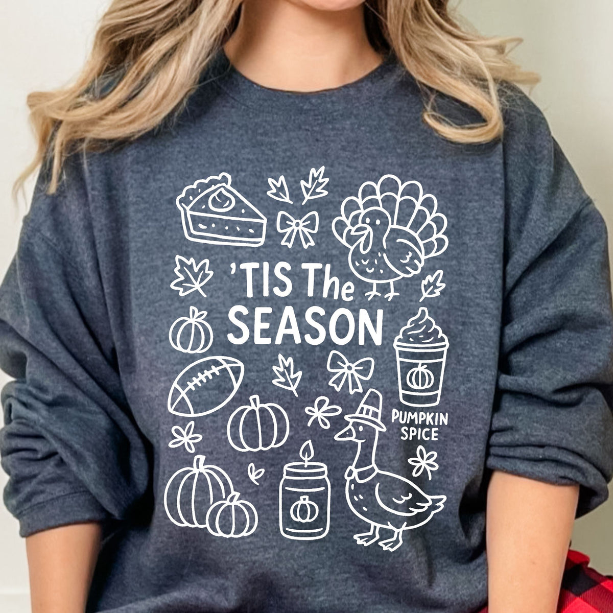 Woman wearing a Dark Heather 'Tis the Season Thanksgiving sweatshirt with white doodle artwork.