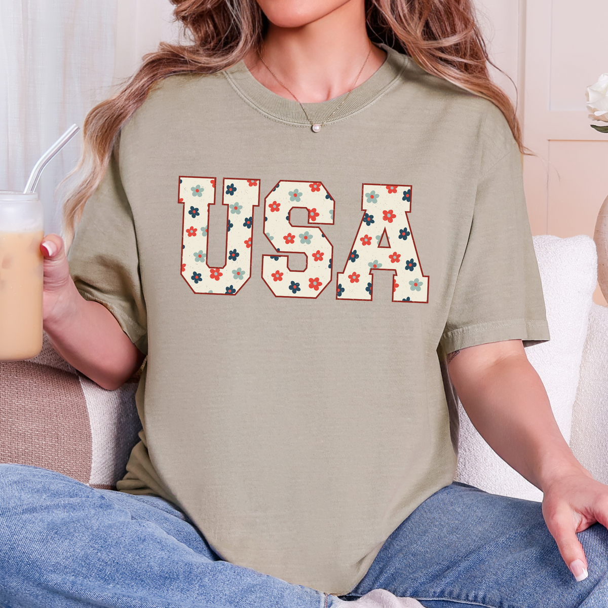 Woman wearing a khaki T-shirt with a floral USA collegiate design.